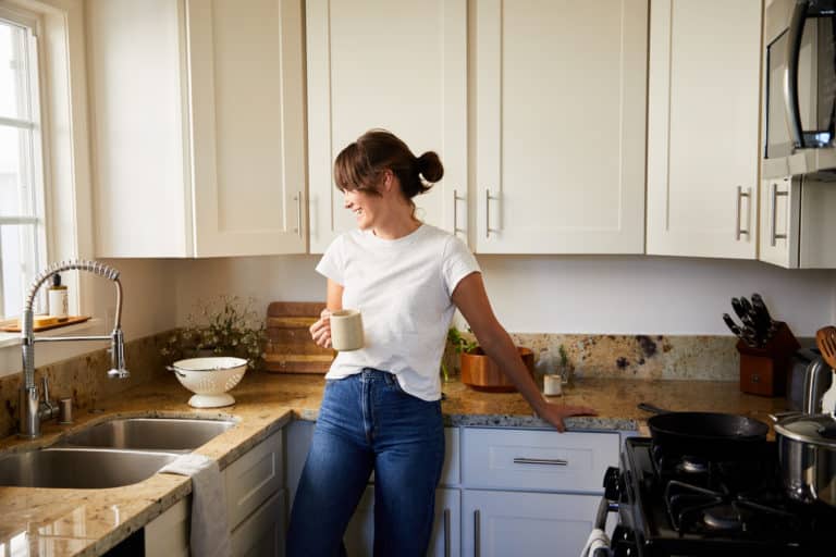 Young woman drinking a cup of coffee and laughing while appreciating her new kitchen at home